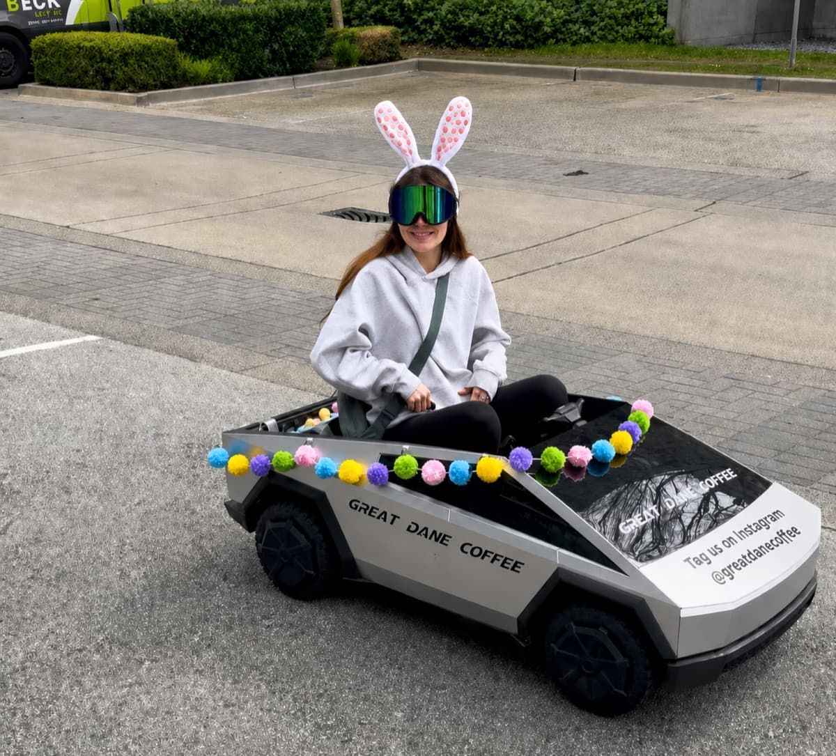 a barista driving the Great Dane Coffee cybertruck in bunny ears on an Easter run